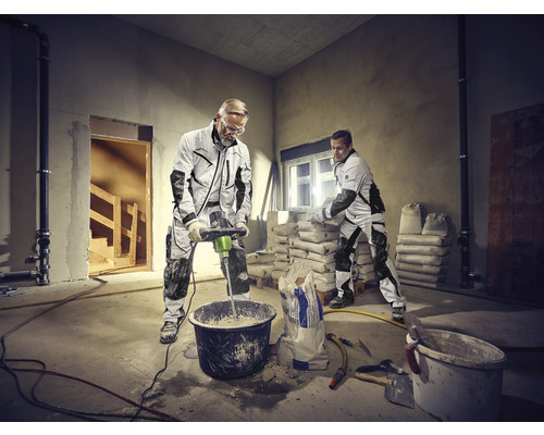 Zwei Handwerker arbeiten in einem Raum mit Sackware und einem Mörtelrührer.