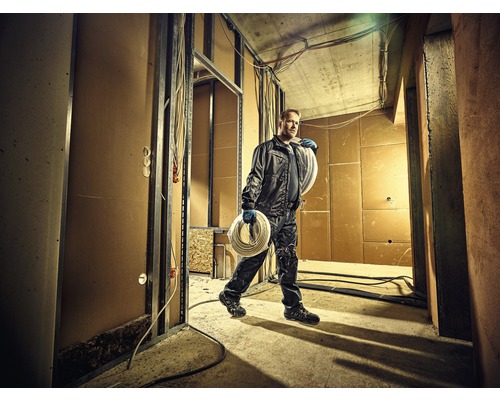 Handwerker trägt Kabelrolle in Rohbau