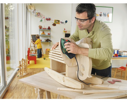 Mann schleift Holzpferd mit Schleifmaschine in Werkstatt