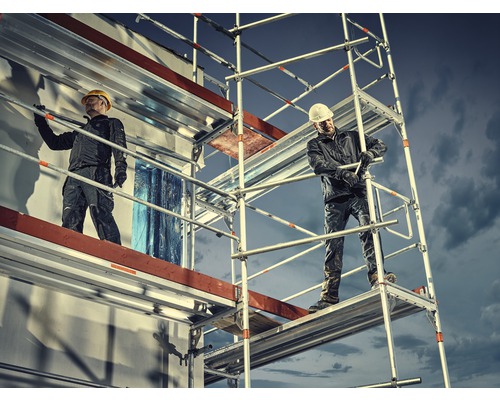 Zwei Handwerker auf einem Baugerüst vor einem Gebäude bei Bauarbeiten.