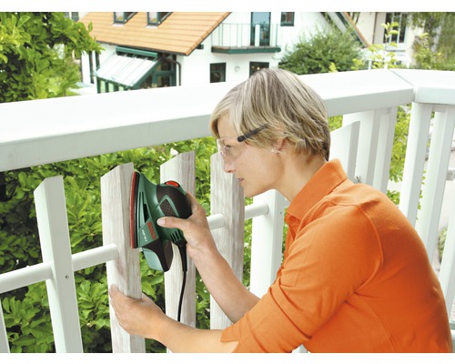 Frau schleift Holzzaun mit einem Schwingschleifer