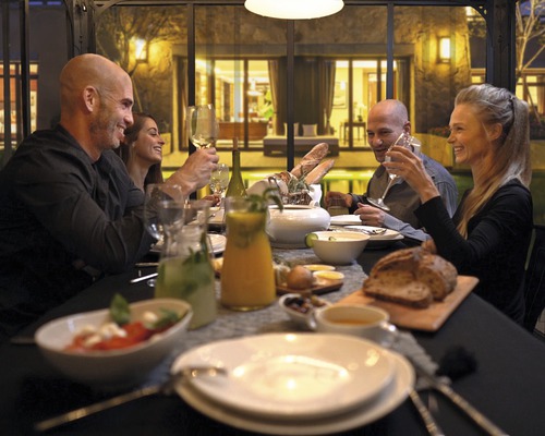 Eine Gruppe von Menschen sitzt an einem gedeckten Tisch und genießt eine Mahlzeit in einer hellen und einladenden Atmosphäre.