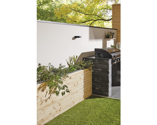 Gestalteter Gartenbereich mit Grillplatz, Holzwand und Grünfläche
