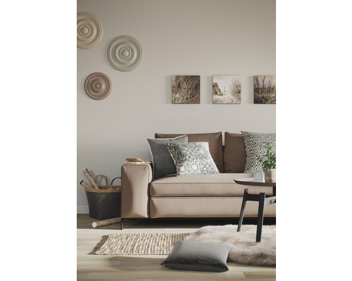Wohnzimmer mit Sofa, Kissen, Teppich und Wanddekorationen in neutralen Farben für ein helles Ambiente.