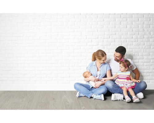 Familie sitzt auf Boden vor einer weißen Ziegelwand