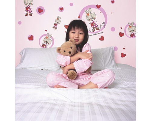 Mädchen mit Teddybär auf einem Bett vor einer Wand mit Wandtattoos.