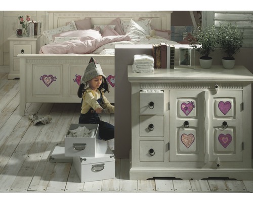 Ein Mädchen spielt in einem Kinderzimmer mit Bett, Nachttisch und Kommode im Landhausstil.