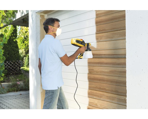 Mann lackiert Holzwand mit Farbsprühsystem