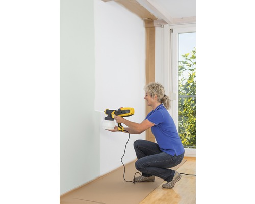 Frau verwendet Farbsprühsystem für Wände in Innenräumen.