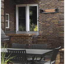 Terrassenszene mit Infrarot-Heizstrahler an Ziegelwand über Gartentisch und Stühlen.