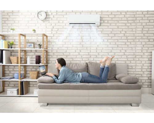 Frau liegt auf Sofa unter Klimaanlage mit Laptop