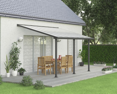 Terrassenüberdachung Palram – Canopia Olympia 3x4.2 425 x 295 cm RAL7016 grau Terrassenüberdachung mit Sitzgruppe auf einer Holzterrasse neben einem Wohnhaus.