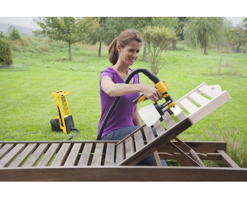 Frau verwendet Farbsprühsystem zum Lackieren einer Holzliege im Garten.