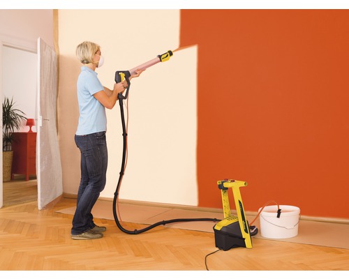 Frau benutzt Farbsprühsystem zum Streichen einer Wand