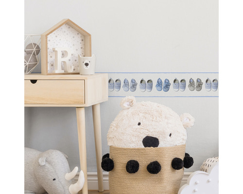 Szene eines Kinderzimmers mit einem Wandbordüren-Muster mit Babyschuhen, einem Holztisch und Stofftieren