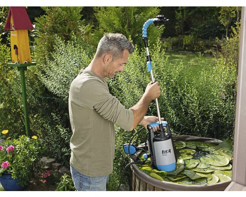Ein Mann benutzt eine Teichschlammpumpe der Marke for.q in einem Gartenteich