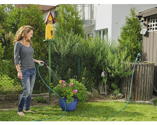 Frau gießt Blumen mit einem Gartenschlauch im Garten.