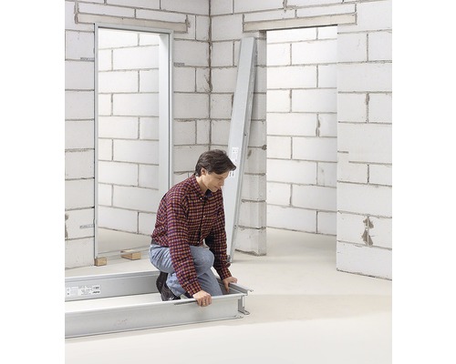 Frau kniet vor Türzargenbausatz auf einer Baustelle mit Betonwänden