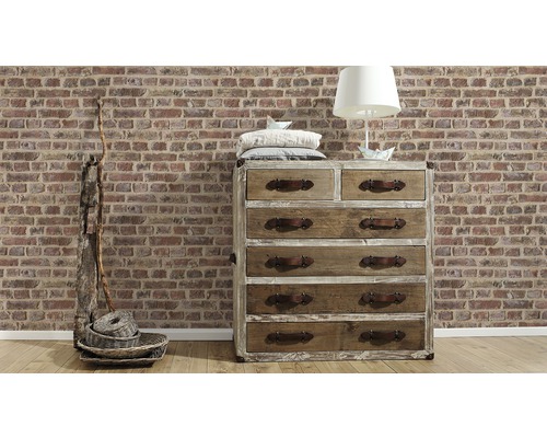 Kommode aus Holz mit Schubladen, Lampe und Dekoration vor einer Ziegelwand