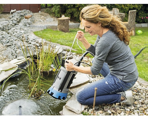 Frau lässt Tauchpumpe in Gartenteich ab