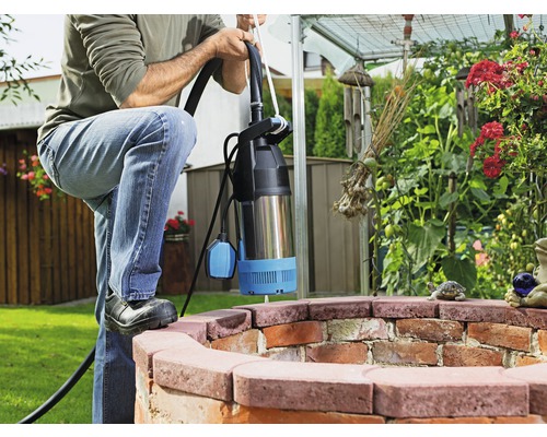 Mann mit Tauchpumpe in einem Gartenbrunnen
