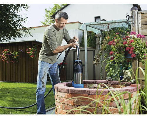 Mann bedient eine Handschwengelpumpe am Brunnen im Garten.