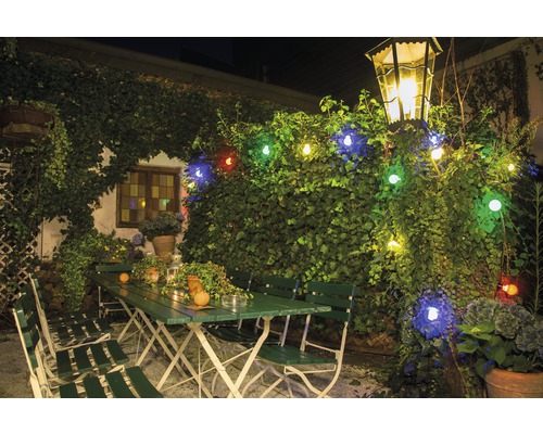Außenbereich mit grünen Gartenmöbeln, beleuchtet mit einer Lichterkette und einer Laterne.