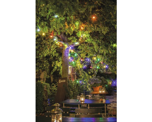 Illuminierter Garten mit Tischen, Stühlen und Laternen unter einem Baum mit Lichterketten.
