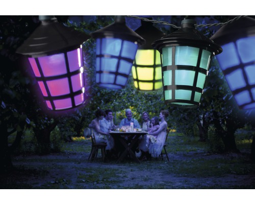 Lichterkette mit bunten Laternen über einer im Garten sitzenden Familie