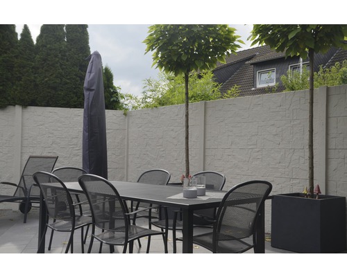 Gartenszene mit Esstisch, Stühlen, Sonnenschirmhülle, Pflanzkübel und Sichtschutzwand