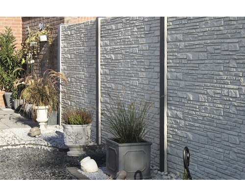 Gartenszene mit Betonzaun und bepflanzten Blumentöpfen.