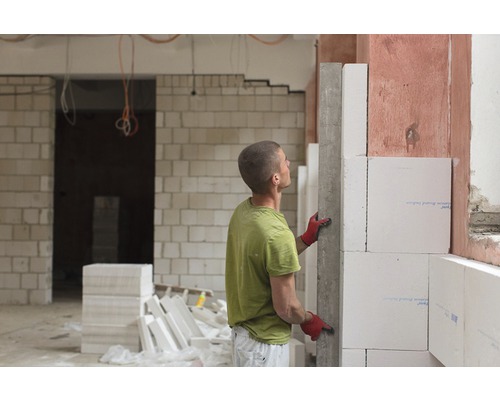 Ein Mann baut eine Wand aus Porenbetonsteinen in einem unfertigen Raum.