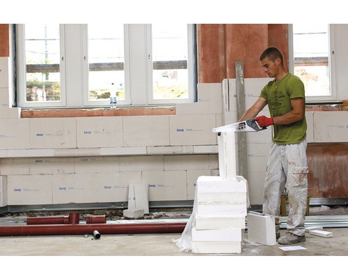 Mann sägt Porenbetonsteine mit einer Säge in einem Raum mit Porenbetonwand