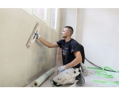 Handwerker trägt Putz mit einer Glättkelle auf eine Wand auf.