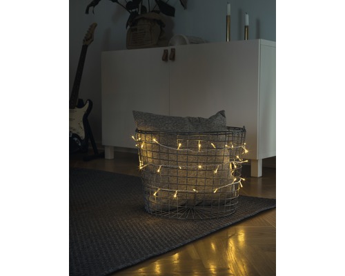 LED Lichterkette Konstsmide 6,93 m + Zuleitungslänge 3 m 100 Micro LEDs Lichtfarbe bernstein t. Kabel Dekorative Szene mit einem Korb, der mit einer Lichterkette und einem Kissen gefüllt ist, auf einem Teppich