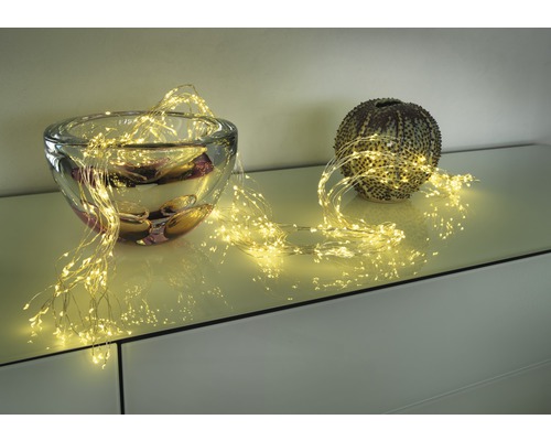 Dekorative Lichterkette drapiert um eine Glasschale und eine Kugelvase auf einem Möbelstück.