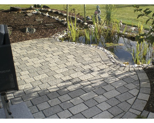 Gepflasterter Gartenweg neben einem Teich mit Gartendekoration
