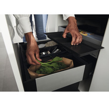 Mülltrennsystem mit mehreren Behältern und einem Deckel, in dem eine Person Grünabfälle entsorgt