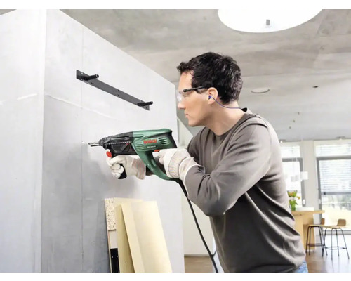Ein Mann bohrt mit einer Schlagbohrmaschine ein Loch in eine Wand.