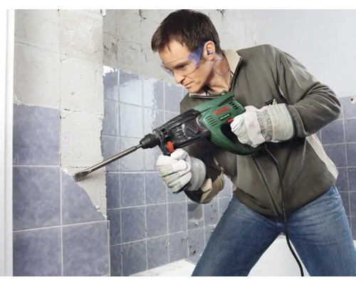 Mann entfernt Fliesen mit einem Bohrhammer in einem Badezimmer.