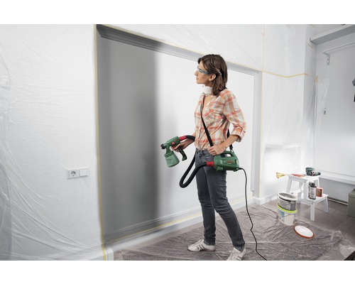 Frau verwendet Farbsprühsystem von Bosch zum Streichen einer Wand im Innenbereich.