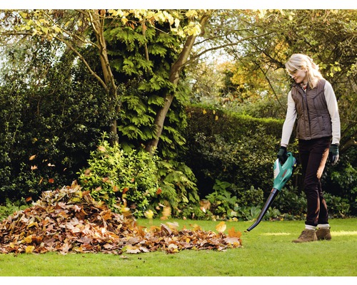 Frau verwendet einen Laubbläser im Garten, um Laub zu entfernen.