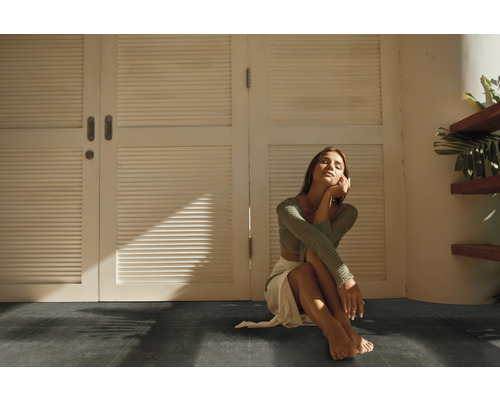 Innenraum mit dunklem Boden und einer Frau, die vor einer weißen Tür sitzt