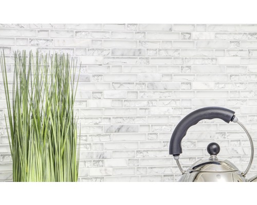 Dekorative Kunstpflanze und Teekessel vor einer Wand aus Mosaikfliesen