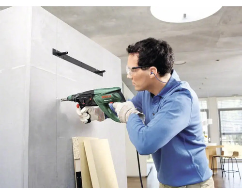 Mann bohrt mit einer Bohrmaschine ein Loch in eine Wand.