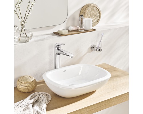 Auf einem Holztisch sind ein Waschbecken, eine Armatur, ein Handtuch und ein Behälter zu sehen.