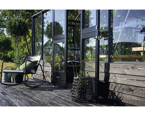 Außenansicht eines Gewächshauses mit Glaswänden, einer Sitzgelegenheit und dekorativen Pflanzen auf einer Holzterrasse