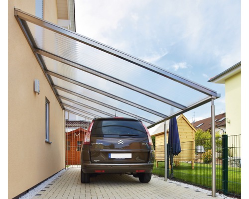 Carport mit Auto auf gepflasterter Fläche vor einem Haus.