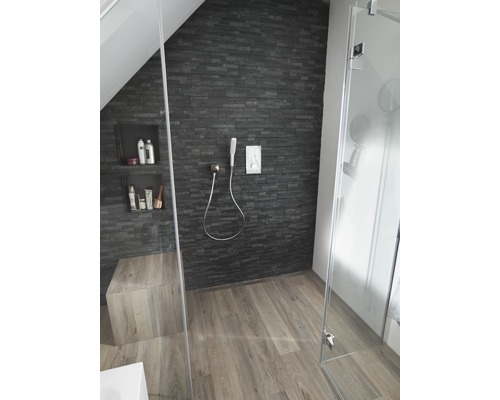 Badezimmer mit Dusche, Steinwand und Holzfußboden.