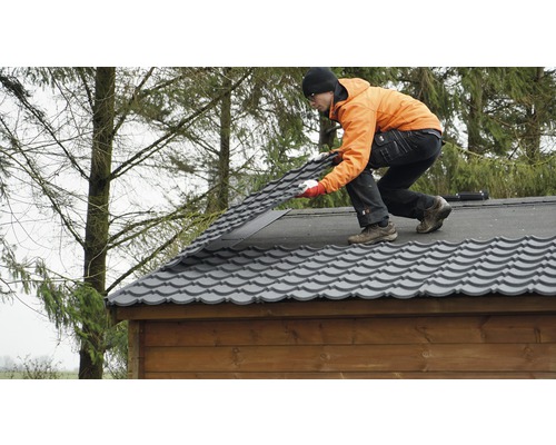 Mann verlegt Metalldachziegel auf einem Holzhaus.